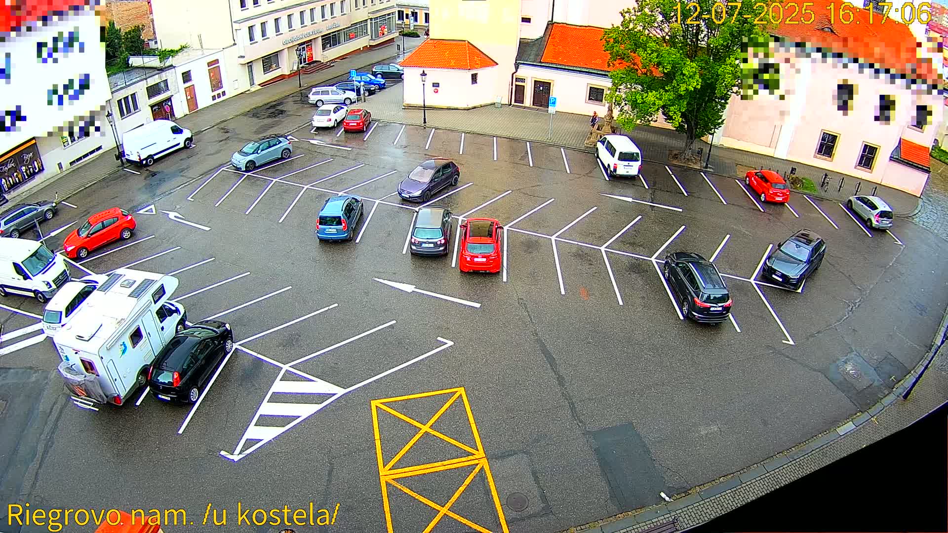 A sunny day reveals a full parking lot with numerous cars parked in spaces, surrounded by buildings.