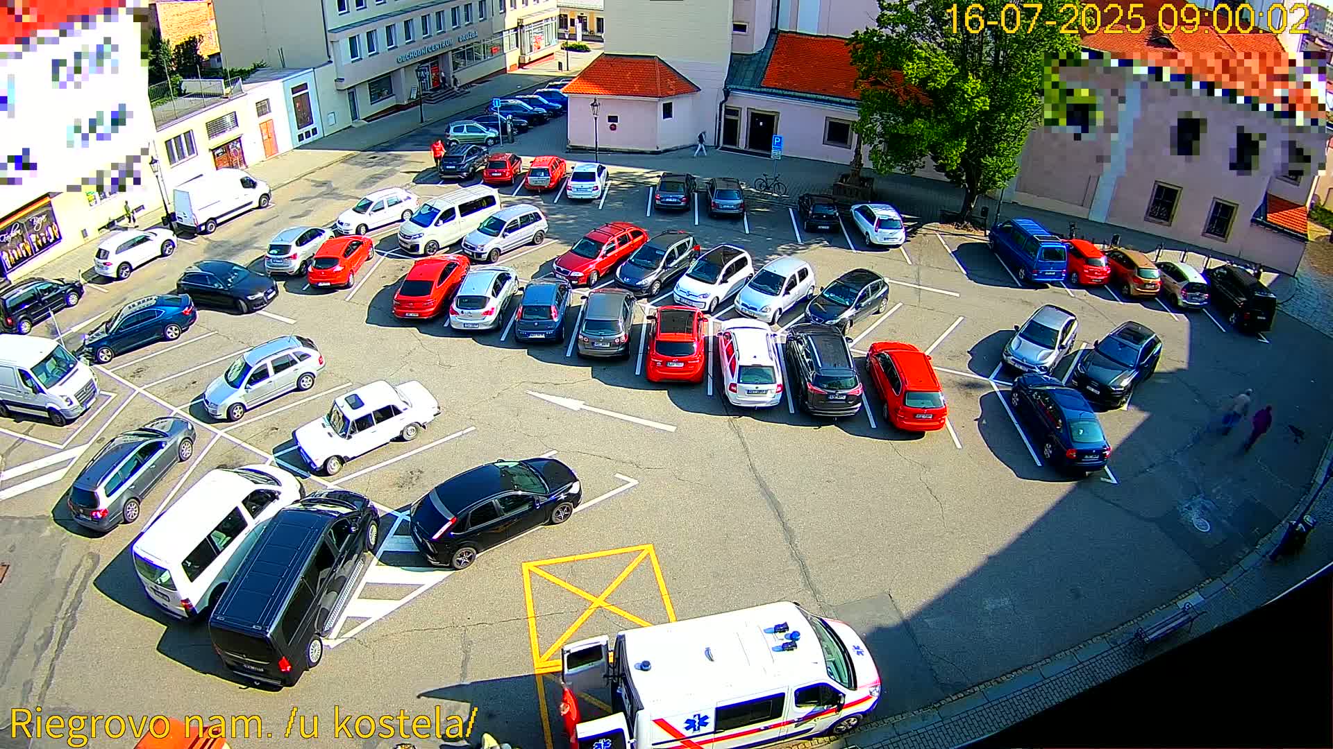 A parking lot filled with numerous cars on a sunny day, with an ambulance partially visible in the bottom right corner.