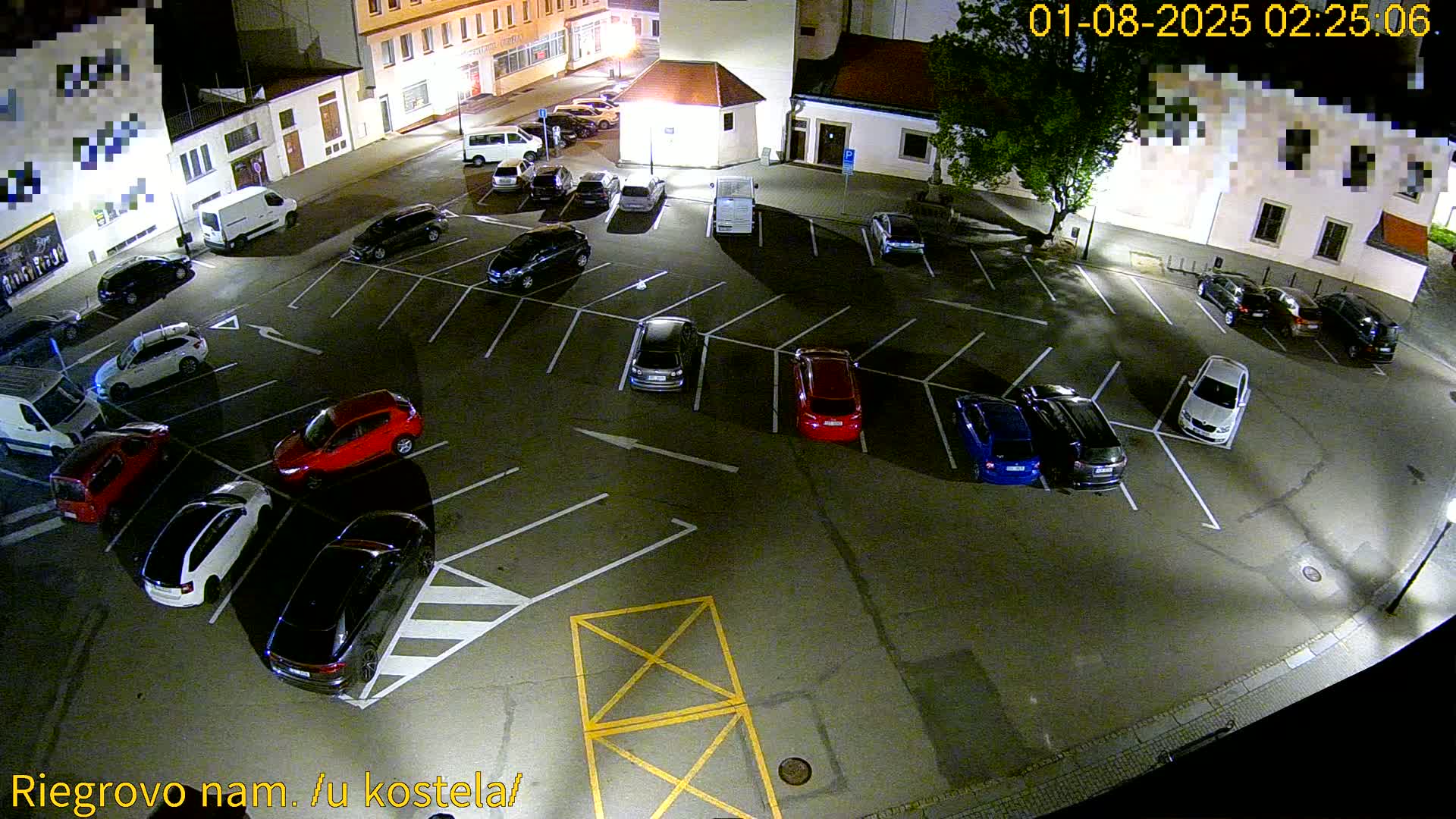 A nighttime aerial view of a mostly empty parking lot with several cars parked in it.