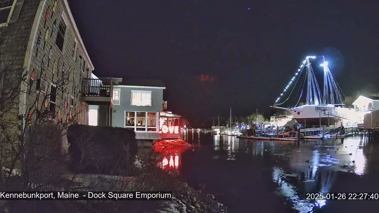 At night, a brightly lit ship is docked in a calm harbor next to buildings, one of which displays a large "LOVE" sign.