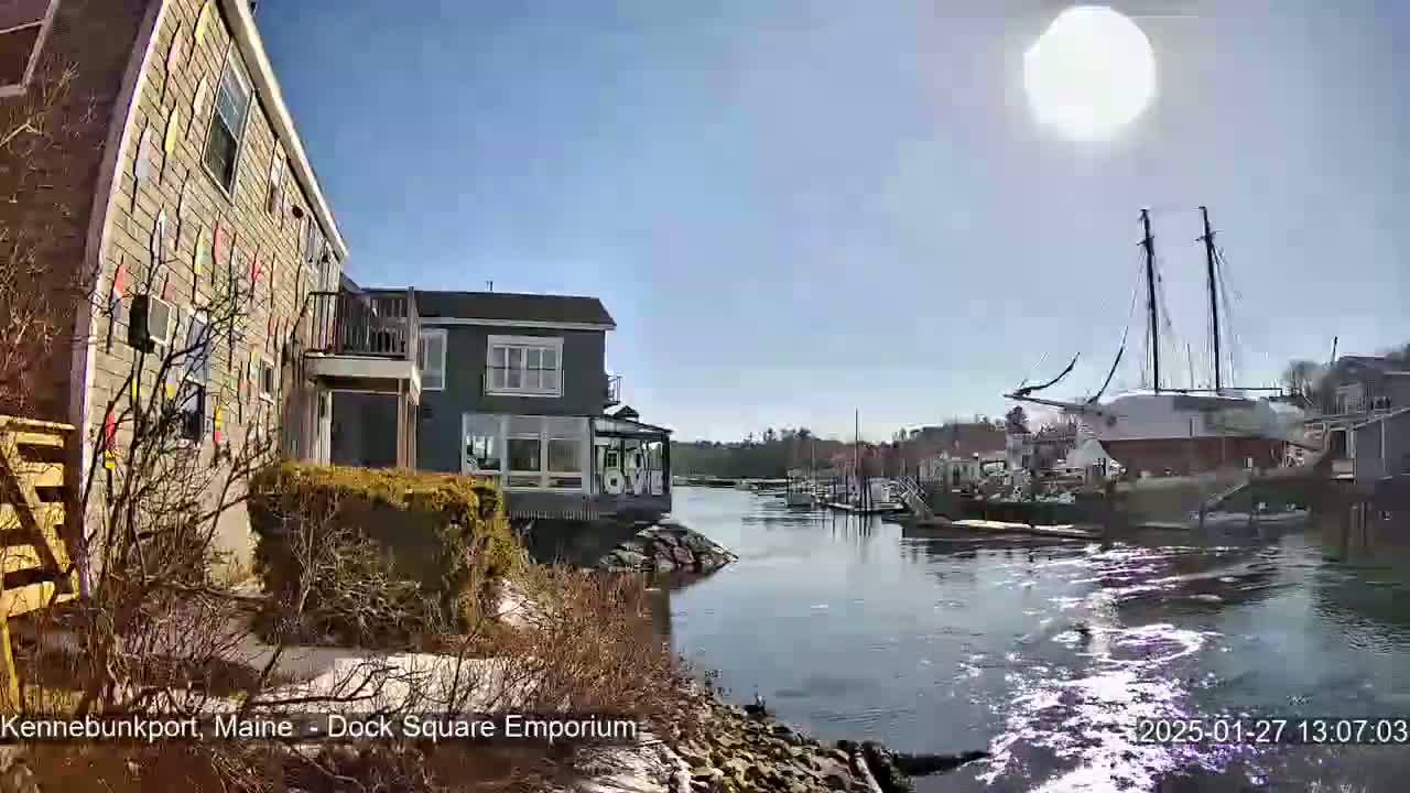 A sunny day reveals a waterfront scene with houses, a large sailboat docked, and calm water.
