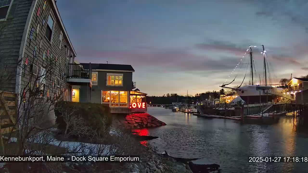 A waterfront scene at dusk shows a building with illuminated windows and a "LOVE" sign, next to a docked sailing ship under a cloudy sky.