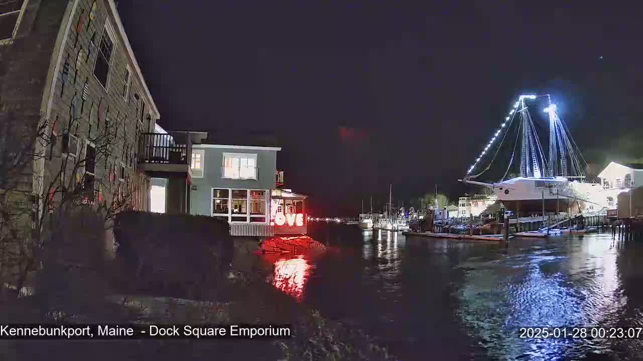 A nighttime harbor scene shows a building with a "LOVE" sign illuminated, a large sailboat docked, and other boats at the pier, under a dark, clear sky.