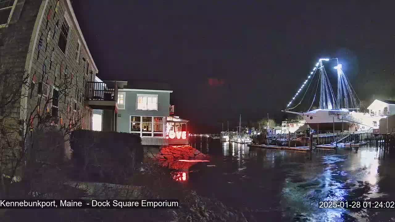 A nighttime waterfront scene shows a building with a "LOVE" sign, a large illuminated ship docked, and calm water reflecting the lights.