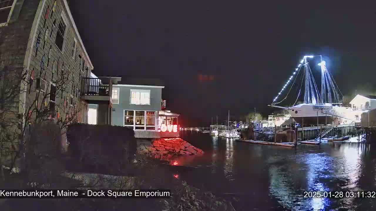 A nighttime waterfront scene shows a large, illuminated sailboat docked near buildings, with a "LOVE" sign glowing red on a rocky shoreline.