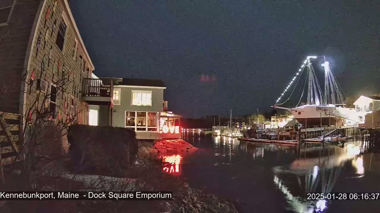 A nighttime waterfront scene shows a building with illuminated "LOVE" letters on the shore, next to a large, illuminated sailboat docked in calm water.