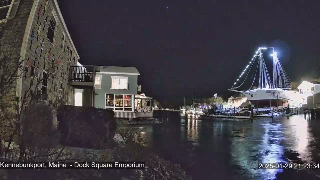 A large, illuminated sailboat is docked at night next to buildings and other boats, under a clear, starry sky.