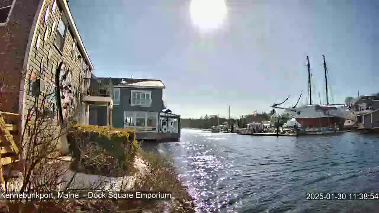 A sunny day shows a waterfront view of houses and a large sailboat docked in a calm waterway.