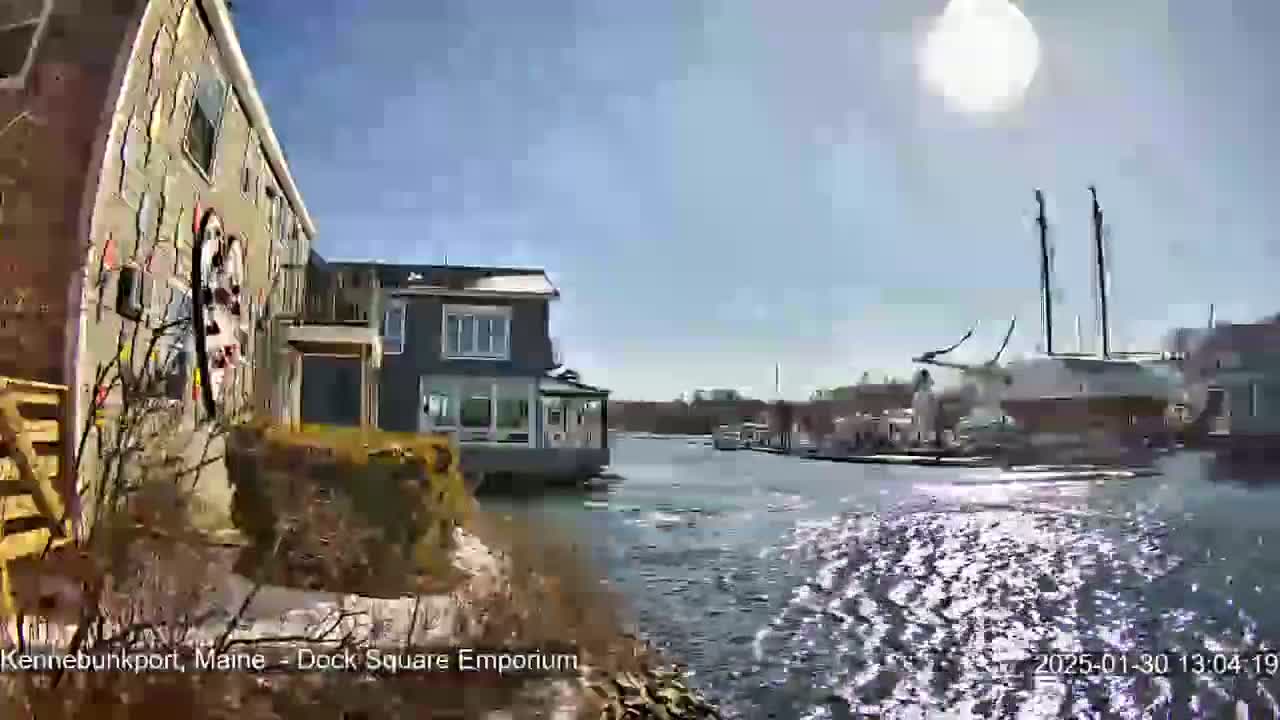 A sunny day shows a waterway with docked boats and buildings along the shore, some of which appear to be residential.