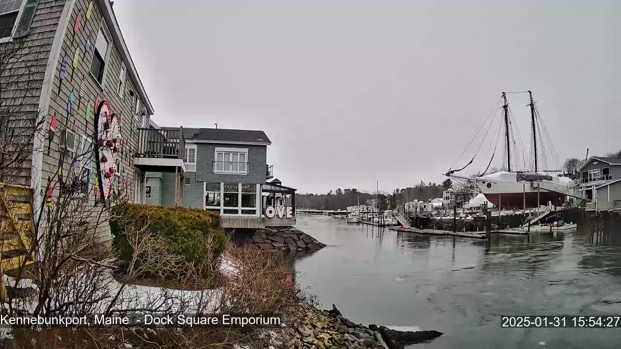 A waterfront view on an overcast day shows a harbor with boats, including a large sailing ship, and buildings, one with a large heart-shaped mural.