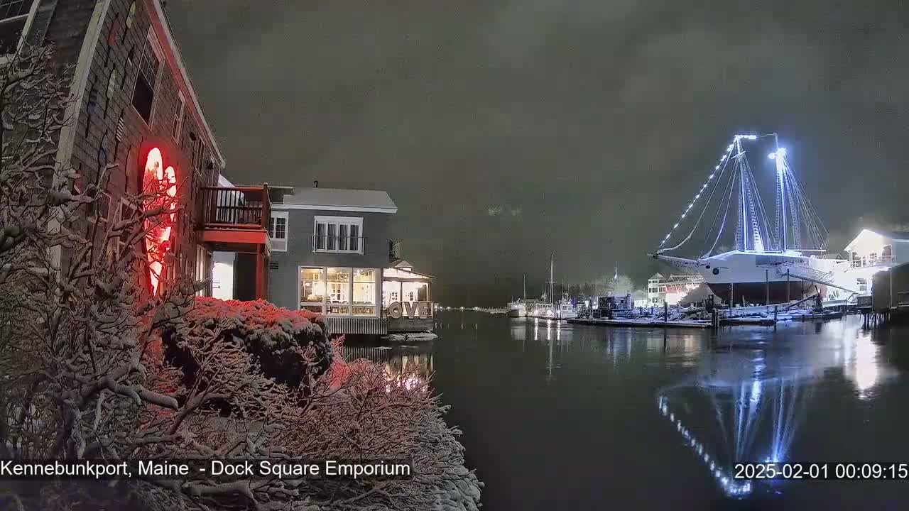 A snow-covered waterfront scene at night shows a large illuminated ship docked near buildings, with a red heart-shaped light visible on one building.