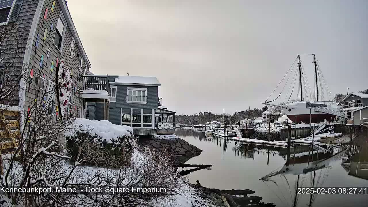 A snow-covered waterfront scene shows a canal with a large docked sailing ship and several buildings, one of which is decorated with colorful pennants.