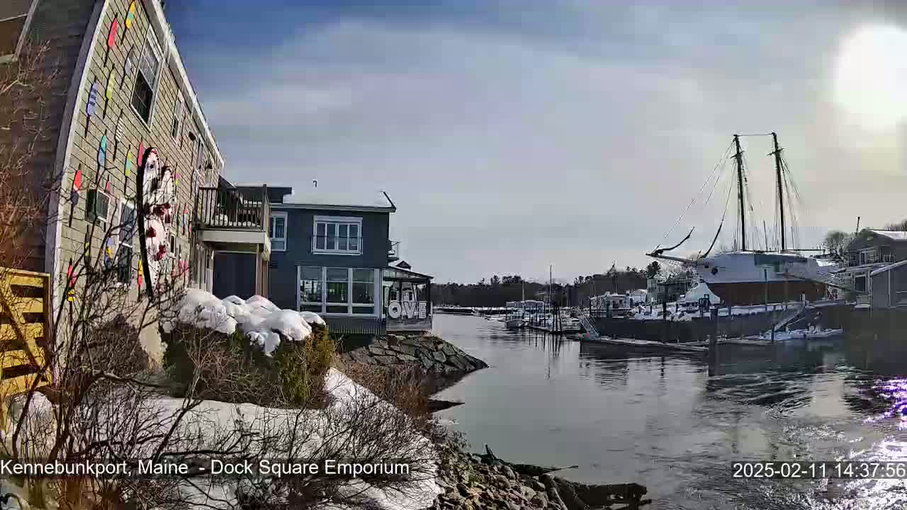 A colorful building with snow-covered landscaping overlooks a harbor with boats docked under a sunny sky.