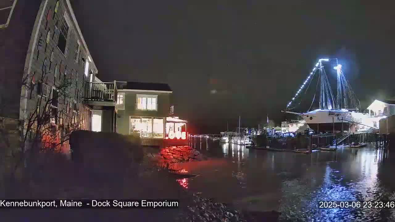 A nighttime view of a waterfront scene with a large illuminated sailing ship docked next to a building, under a dark sky.