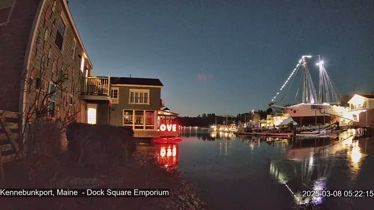 A large sailboat is docked at night next to waterfront buildings, one of which displays illuminated "LOVE" letters, under a clear, dark sky.