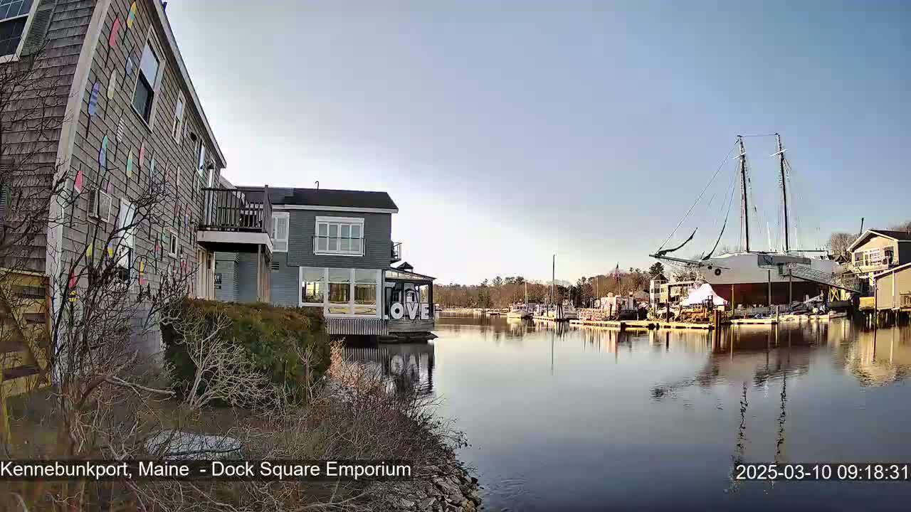 A calm, clear day reveals a waterfront scene with buildings, docked boats, and a large sailing ship.