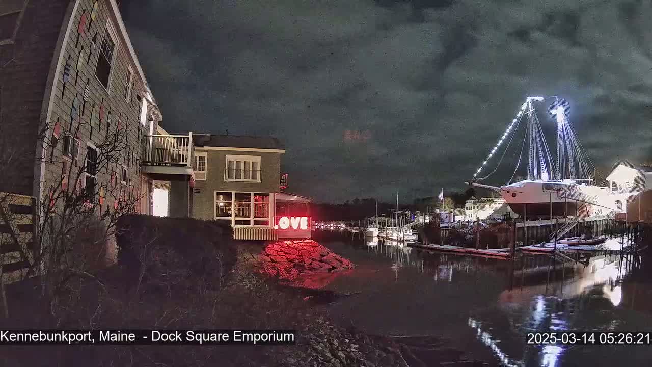 A nighttime harbor scene shows a large sailboat illuminated, docked near a building with a "LOVE" sign, under a partly cloudy sky.