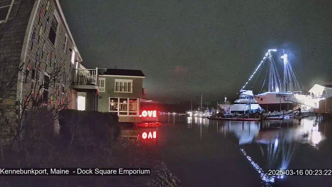 A nighttime waterfront scene shows a building with a "LOVE" sign near a docked sailboat under a dark, cloudy sky.