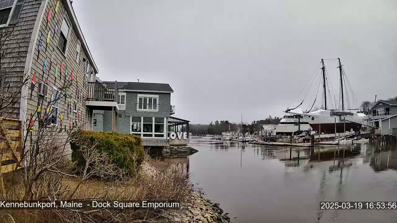 A gray day reveals a waterfront scene with a building decorated with colorful pennants, another building displaying large letters spelling "LOVE", and a large sailboat docked in calm water.