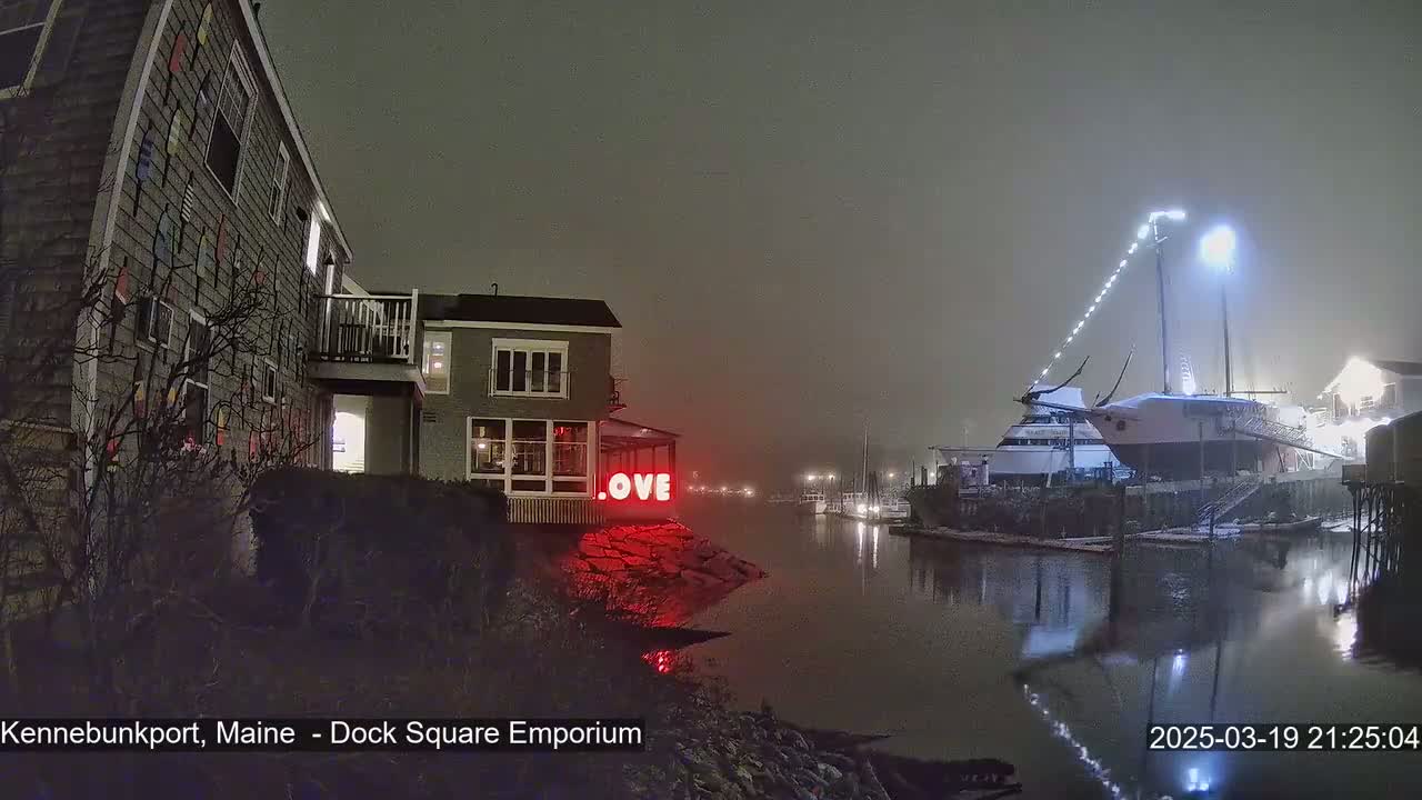 A nighttime, foggy scene shows a building with a red "LOVE" sign next to a calm body of water where boats are docked.
