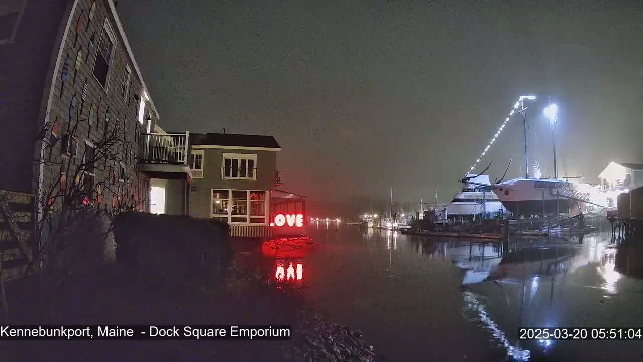A nighttime scene of a harbor with a building displaying a red "LOVE" sign, a sailboat docked, and foggy conditions.
