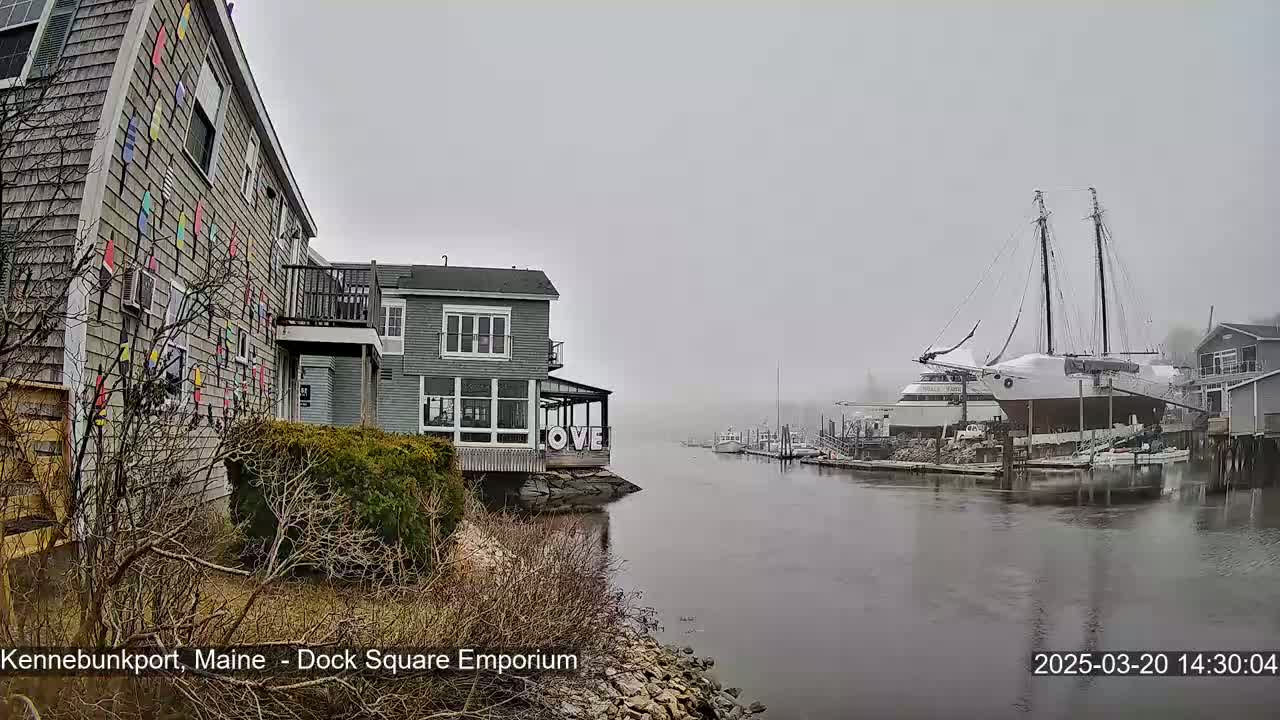 A foggy waterfront scene shows a building adorned with colorful paddles, another building displaying the word "LOVE," and a large sailboat docked in the harbor.