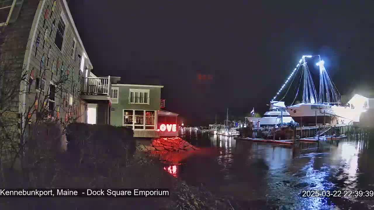 A brightly lit sailboat is moored at a dock next to a building with a colorful exterior at night.