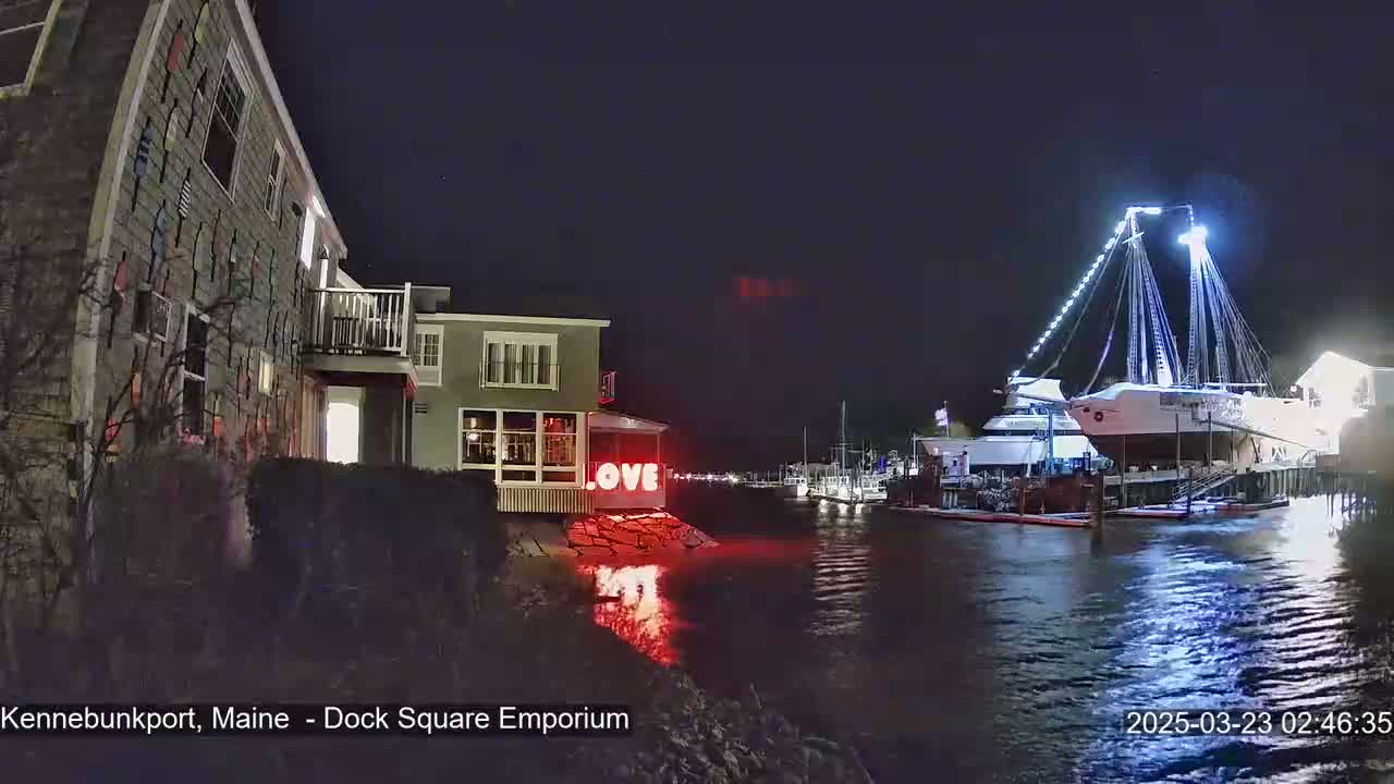 A nighttime waterfront scene shows a building with a "LOVE" sign illuminated in red, next to a body of water where a large ship is docked under bright lights.