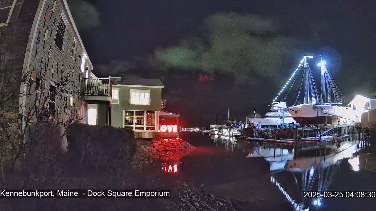 A nighttime harbor scene shows a building with nautical-themed siding, a large illuminated sailboat on a dock, and red "LOVE" letters on a nearby rock.