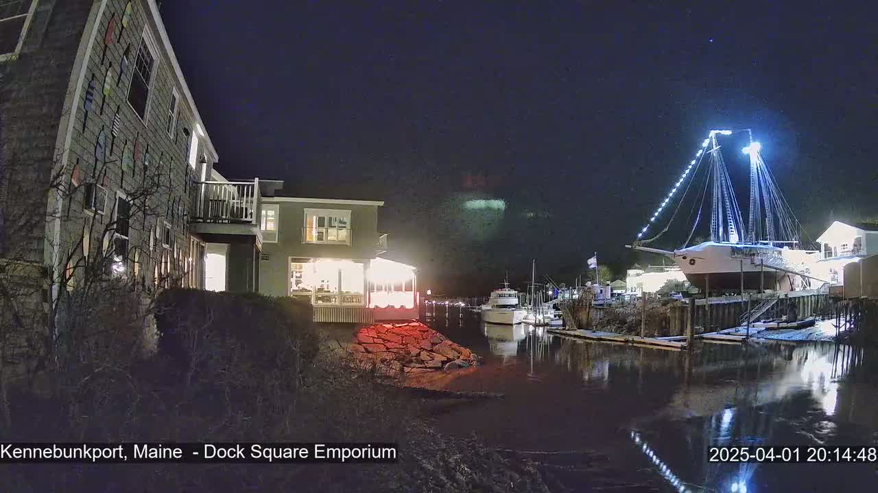 A large, illuminated sailboat is docked at night next to a building and other boats, under a clear, dark sky.