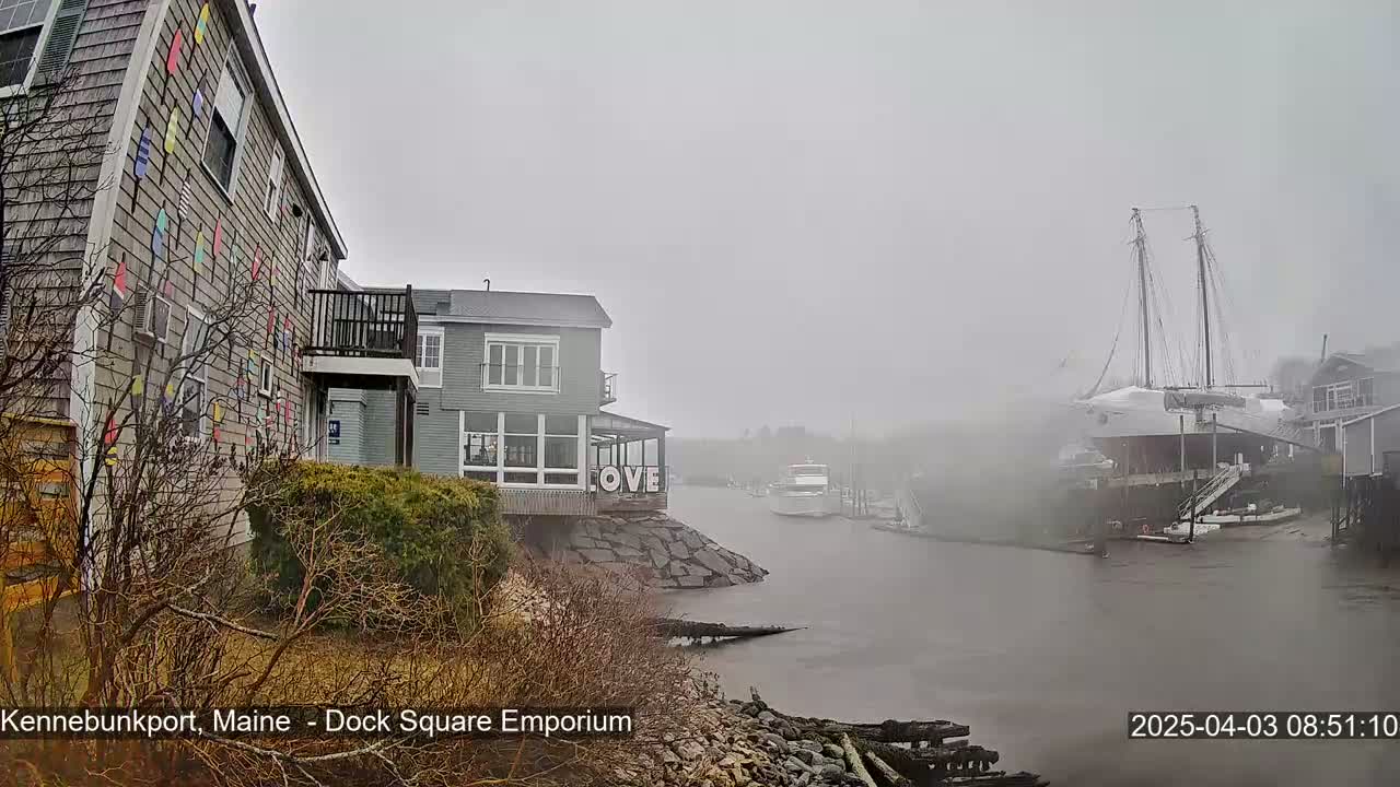 A foggy waterfront scene shows a building decorated with colorful pennants, another building with a "LOVE" sign, and a large sailboat docked nearby.