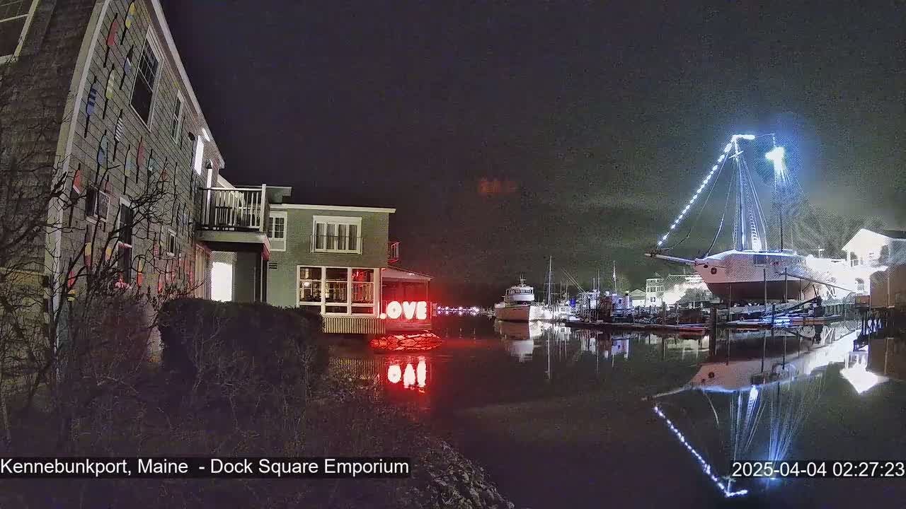 At night, a harbor scene shows a building decorated with nautical-themed siding, illuminated "LOVE" letters near the water, and a large sailboat lit up at a dock, all reflected in calm water.