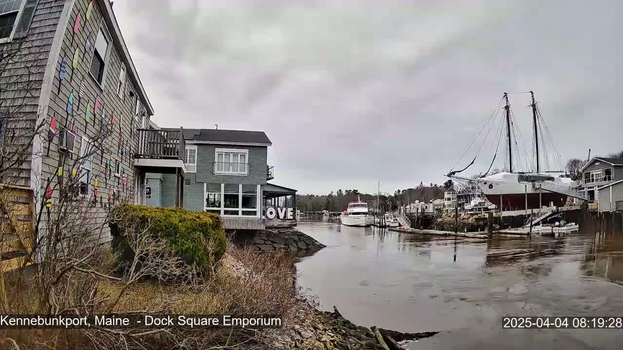 A waterfront scene on an overcast day shows a gray building adorned with colorful nautical flags, another building with a sign that says "LOVE," and a large sailing ship docked nearby.