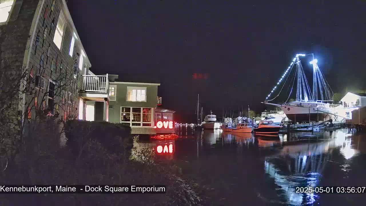 A nighttime harbor scene shows a large sailboat illuminated with lights, several smaller boats, and buildings along the waterfront, with "LOVE" displayed in lights near one building.
