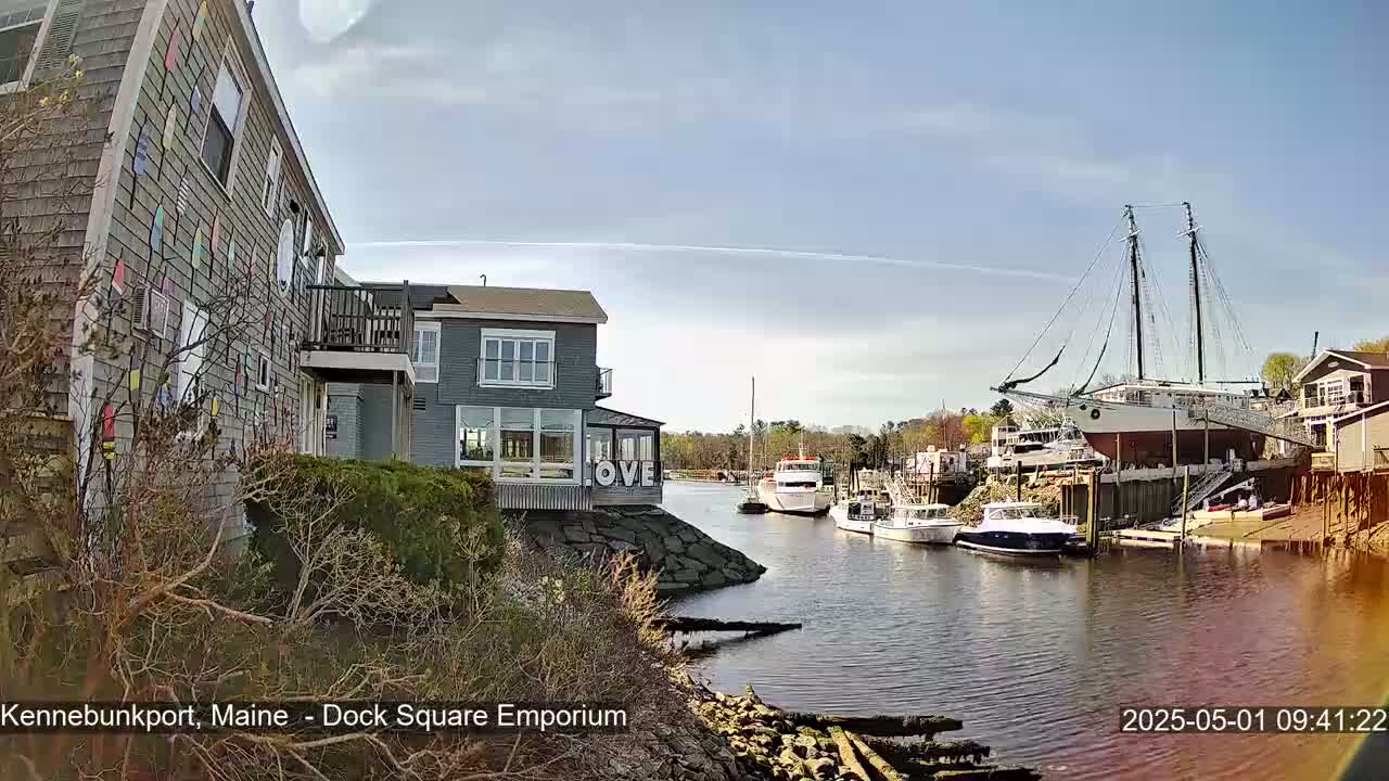 A waterfront scene on a sunny day shows buildings, docked boats, and a large sailing ship resting on supports.