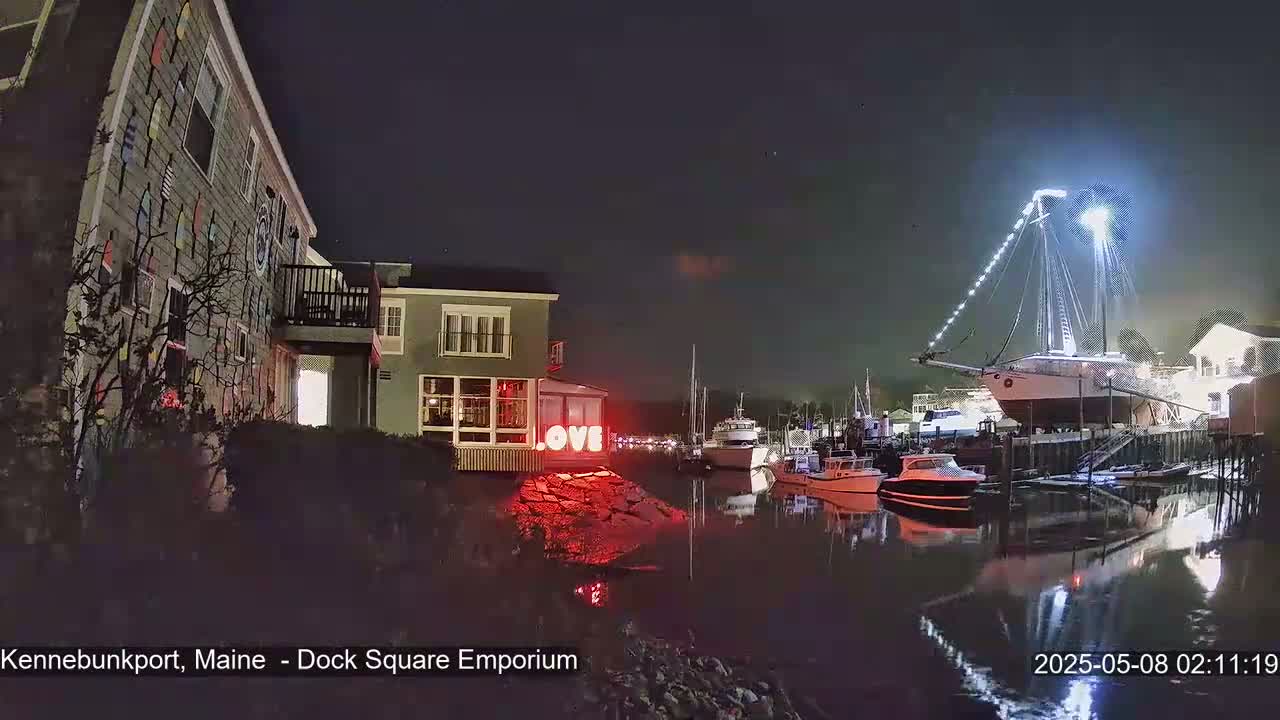 A brightly lit sailboat is docked at night next to a building with a "LOVE" sign, other boats are in the harbor, and the scene is illuminated by lights.
