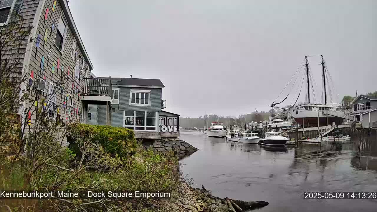 A gray, overcast day shows a harbor with several boats, including a large sailing ship docked, and buildings with colorful exterior decorations along the water's edge.