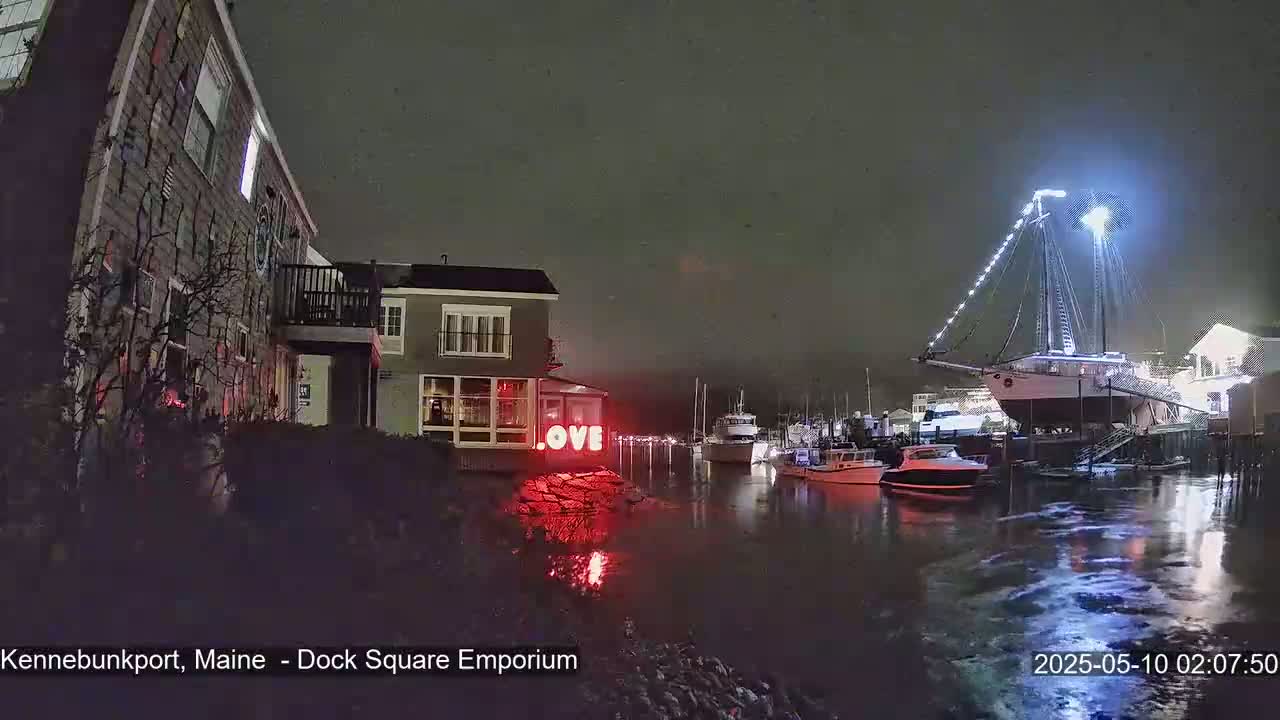 A nighttime view of a harbor with boats, buildings, and a lighted "LOVE" sign, under snowy conditions.
