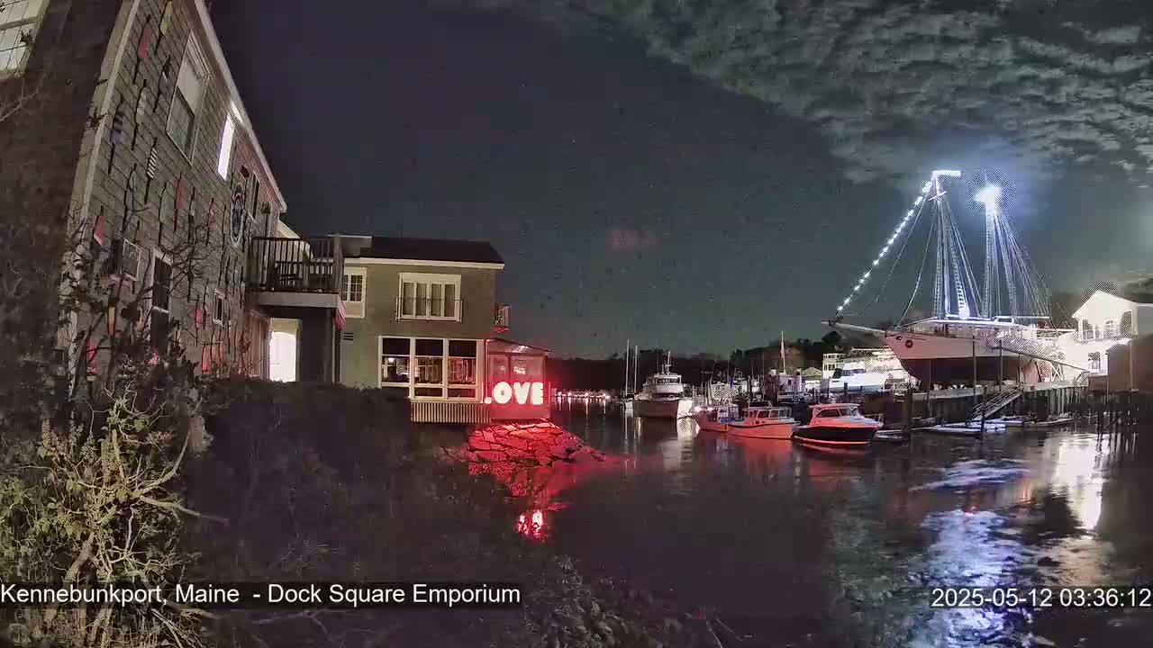 A nighttime harbor scene shows a large sailboat illuminated, several smaller boats moored nearby, buildings on the shore, and a red "LOVE" sign on a small rocky outcropping.