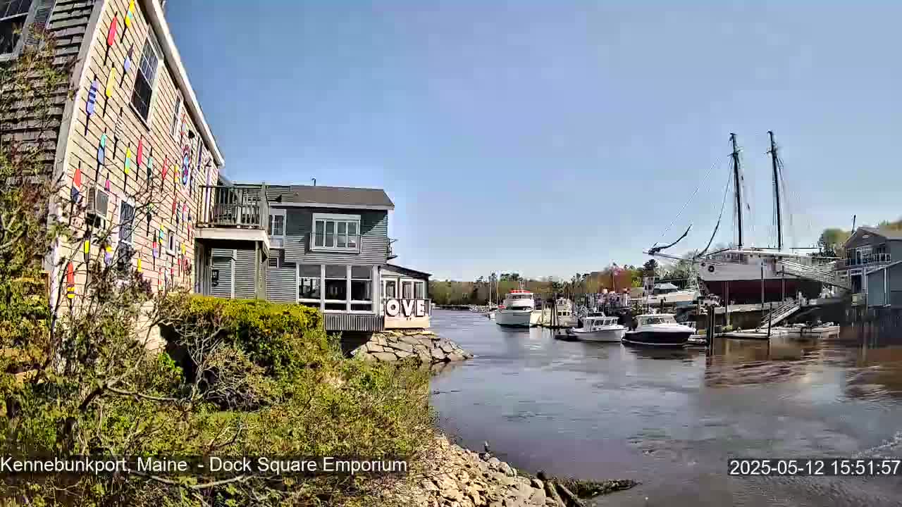 A sunny day shows a waterfront scene with buildings, boats docked, and a large sailing ship on dry land.
