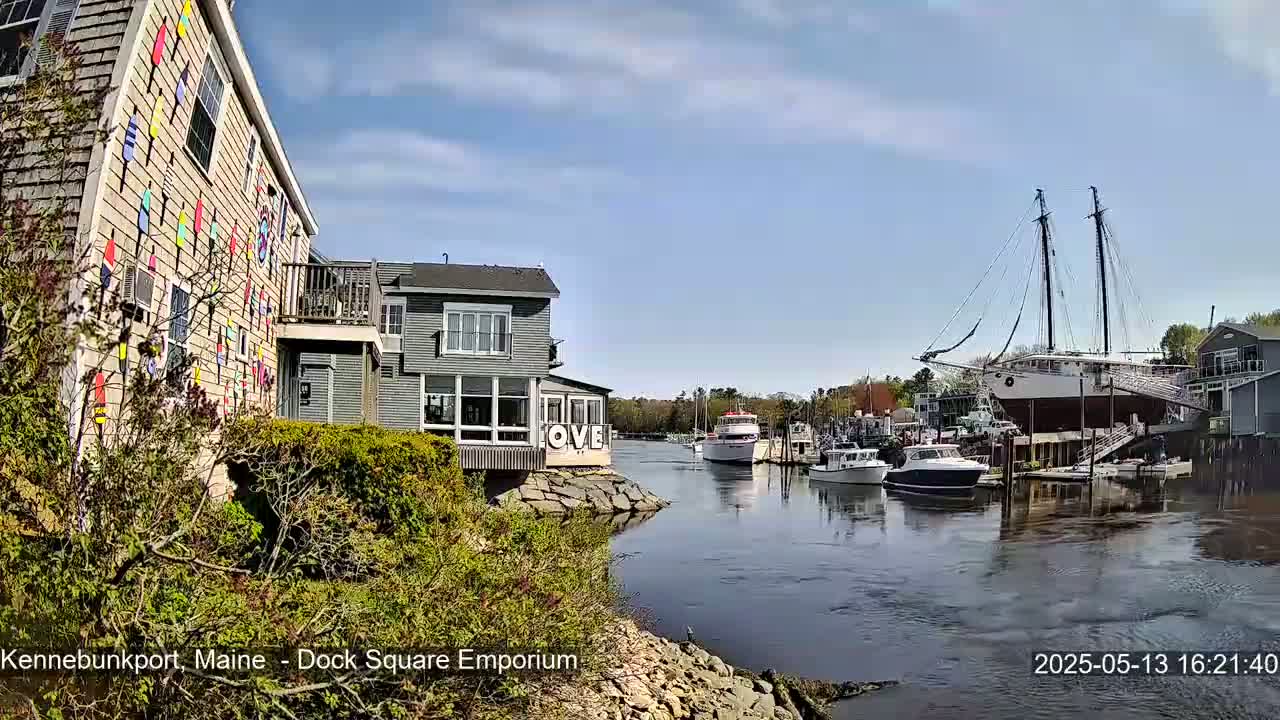 A colorful building sits beside a calm waterway where several boats are moored, under a mostly sunny sky.