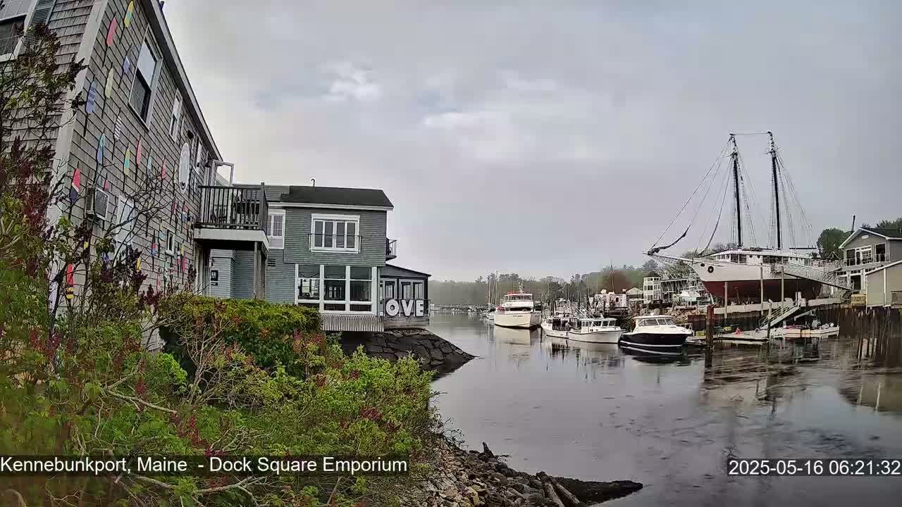 A harbor scene on an overcast day shows several boats, including a large sailing vessel, moored near buildings, one of which displays a large "LOVE" sign.
