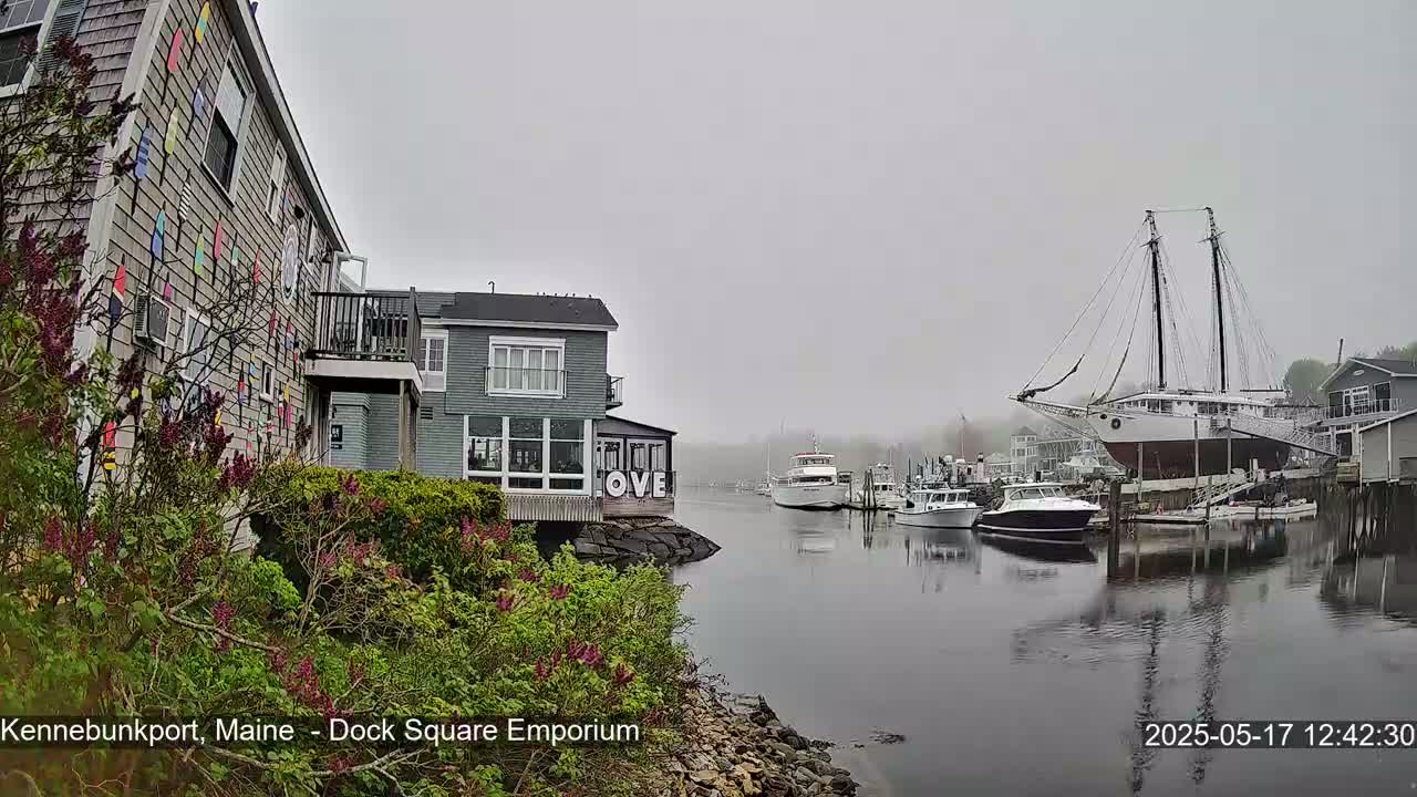 A foggy harbor scene shows a building with colorful decorations, several boats, and a large sailing ship docked.