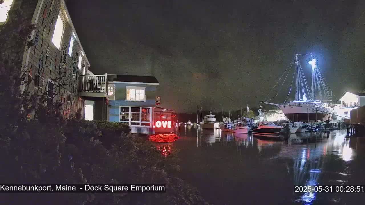 At night, a waterfront scene shows a building with a red "LOVE" sign near a harbor where several boats are docked, including a large sailing ship illuminated by lights.
