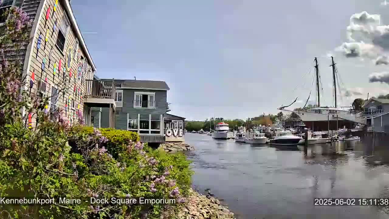 A calm waterway with several boats, including a large sailboat, is seen from a waterfront perspective, under a partly cloudy sky.