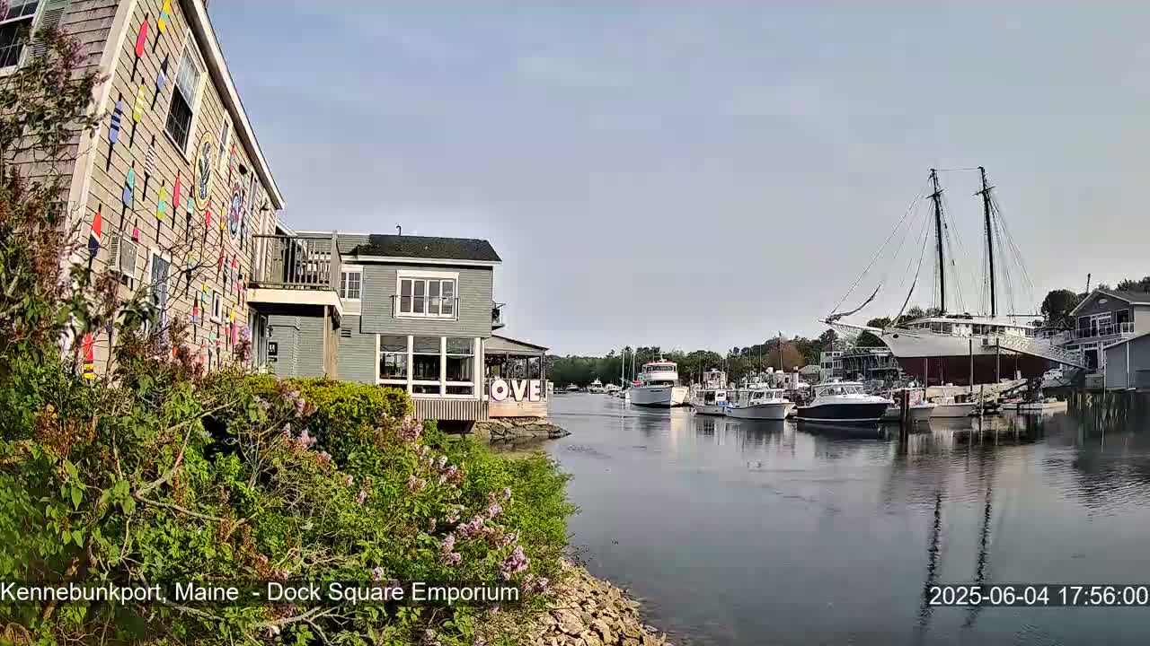 A calm waterway shows several boats and buildings on a sunny day, one building decorated with colorful nautical flags.
