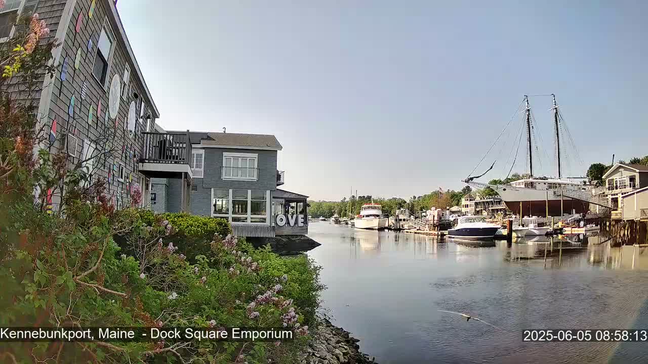 A waterfront view on a sunny day shows a colorful building, other buildings, several boats and a large sailing ship docked at a marina.