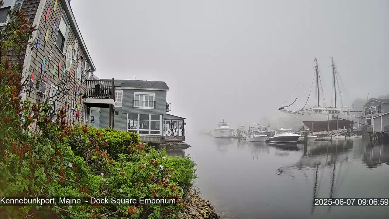A foggy harbor scene shows several boats, including a large sailing ship, moored near waterfront buildings.