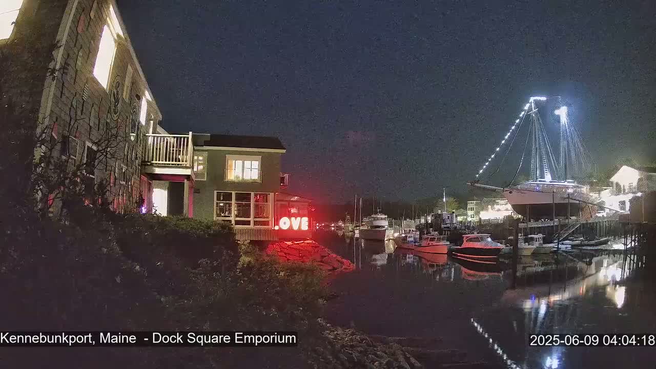 At night, a harbor scene shows a building lit with a "LOVE" sign, other buildings, boats moored in the water, and a large sailboat brightly lit on a dock.