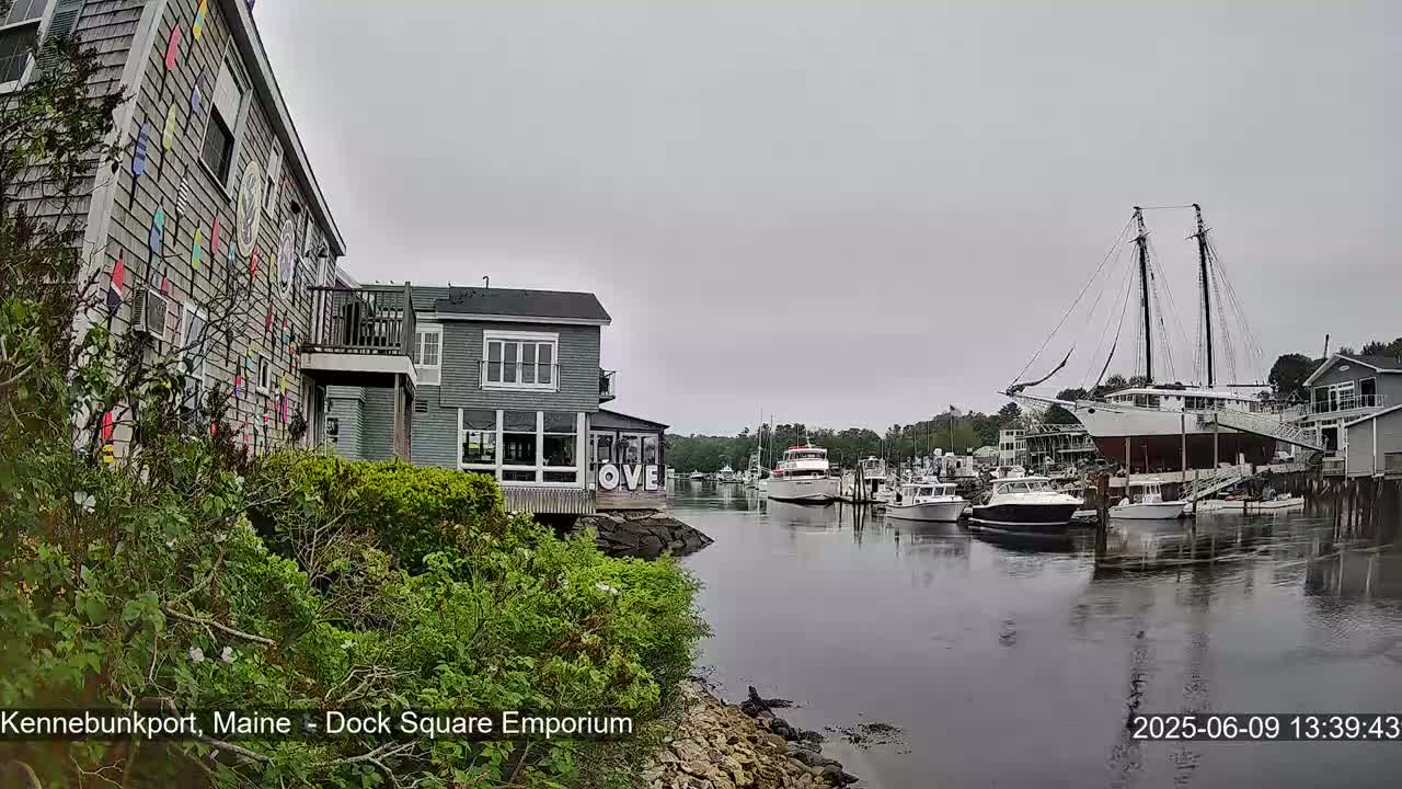 A harbor scene on an overcast day shows several boats, including a large sailing ship, docked near buildings with colorful exterior decorations.